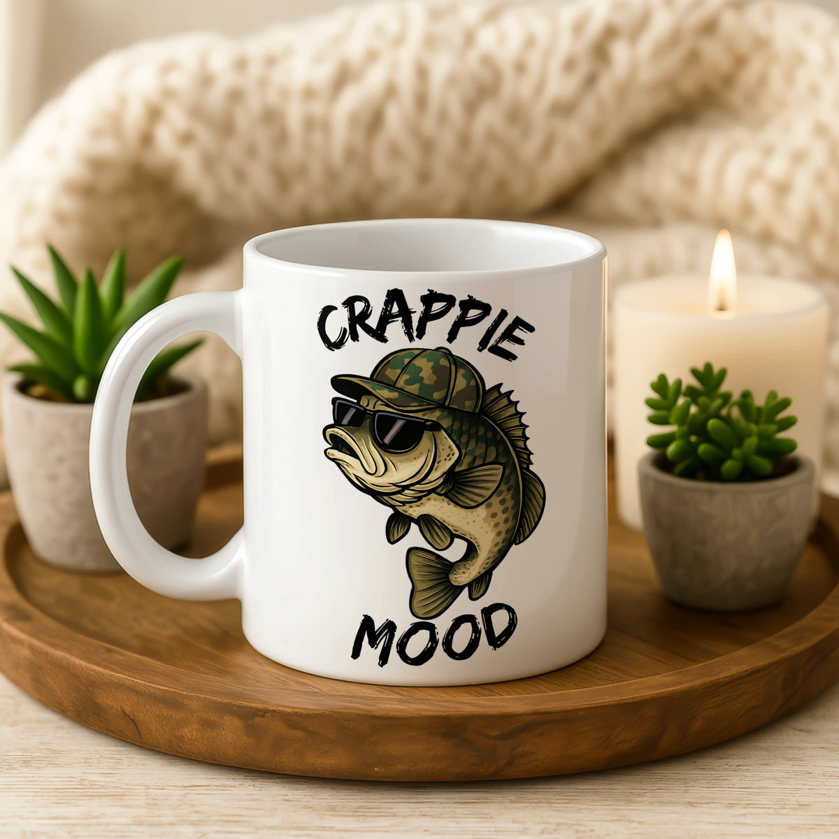 White mug with fish design and 'Crappie Mood' text on a wooden tray with plants and a candle.
